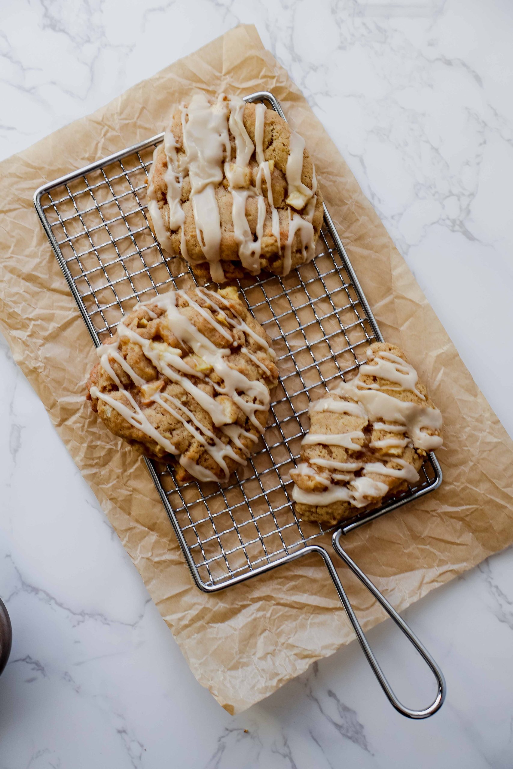 apple fritter cookie with a maple glaze on a cooling rack and parchment paper